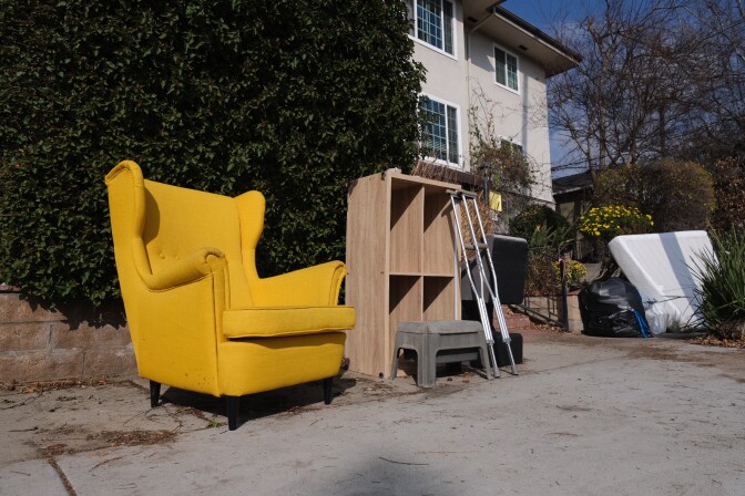 A bright yellow chair, a bookcase, crutches and a mattress are among the items piled on a sidewalk outside an apartment building near the Eaton Fire burn area. 