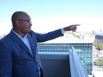 Long Beach Mayor Rex Richardson, the board chair of LACAHSA, stands on a city hall balcony and points to a housing project under construction.