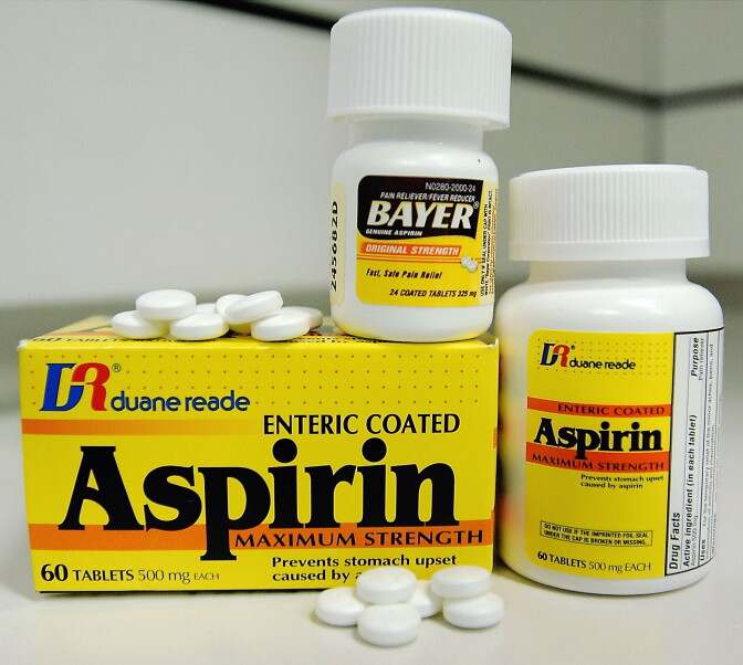 A box of aspirin and two bottles of aspirin, with several pills on top and in front of the box. 