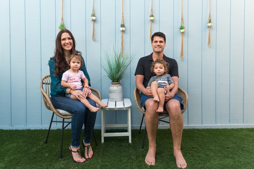 Two parents holding their children in chairs by a plant