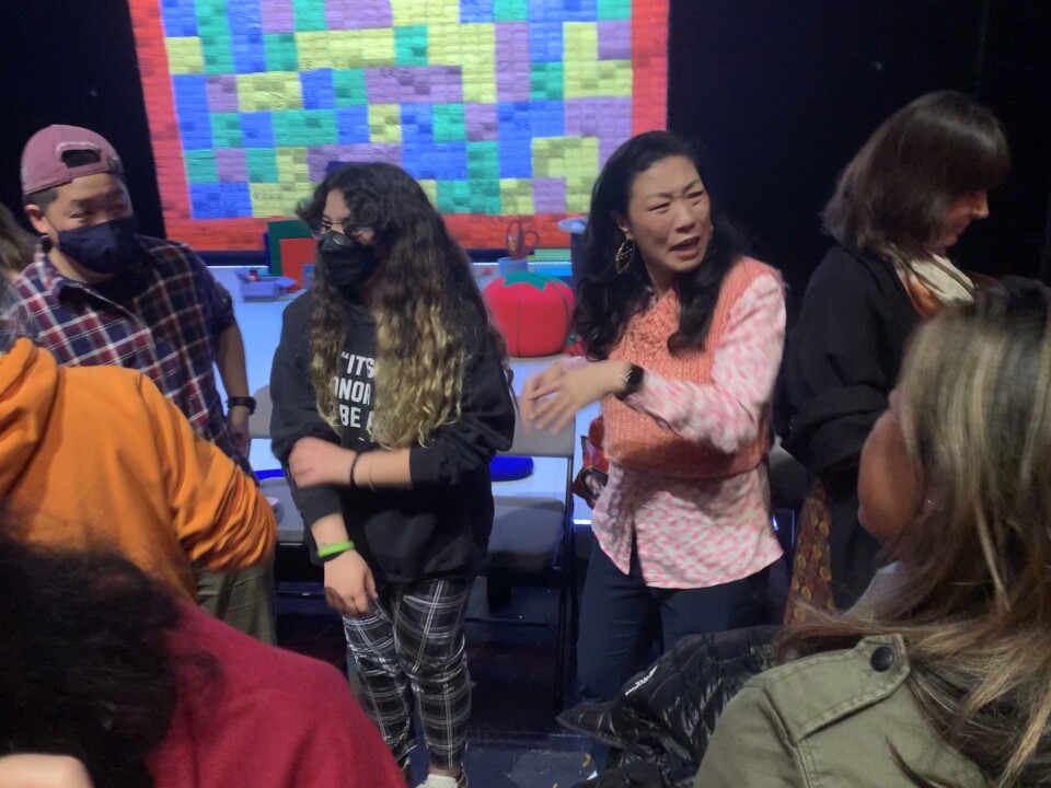 Audience members surround performer Kristina Wong, wearing a pink sweater vest after her show. 