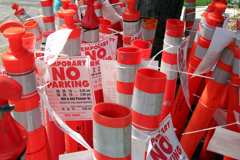  A group of traffic cones are clustered together. Many have "no parking" signs taped to them.