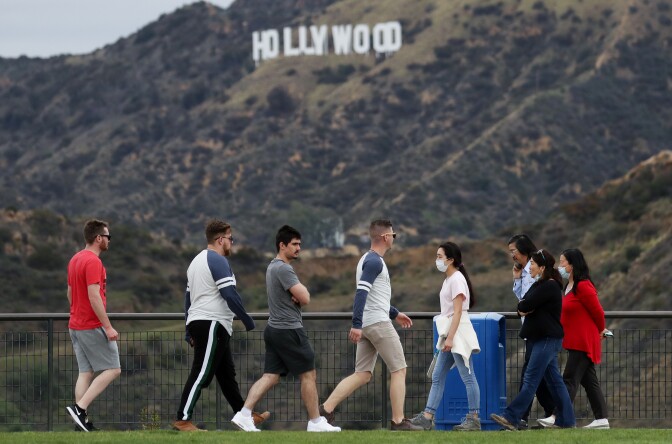 LOS ANGELES, CALIFORNIA - MARCH 22: People, some wearing face masks, walk in Griffith Park with the Hollywood sign behind them on March 22, 2020 in Los Angeles, California. California Governor Gavin Newsom issued a ‘stay at home’ order for California’s 40 million residents in order to slow the spread of coronavirus (COVID-19). Californians may still visit parks without violating Newsom’s order as long as they maintain social distancing and adhere to other public health measures related to the coronavirus. Los Angeles Mayor Eric Garcetti today urged Angelenos to practice physical distancing after crowds were seen at some beaches and hiking trails this weekend.  (Photo by Mario Tama/Getty Images)