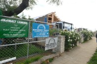 Fencing lines a sidewalk next to a home under construction. Signs on the fence bear the Horusicky name.
