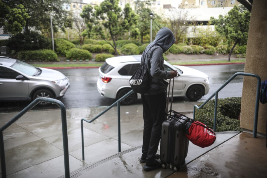 A student stands with his belongings while moving out of his dormitory at San Diego State University