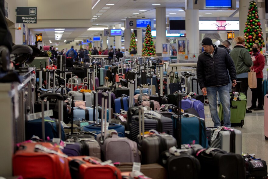 Scores of suitcases are piled tightly together as people look for their bags inside an airport.