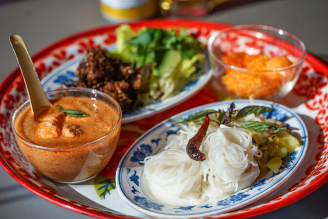 Four Thai dishes, including a noodle dish, curry and a duck yolk and sugar dessert, rest on a larger red and white plate.