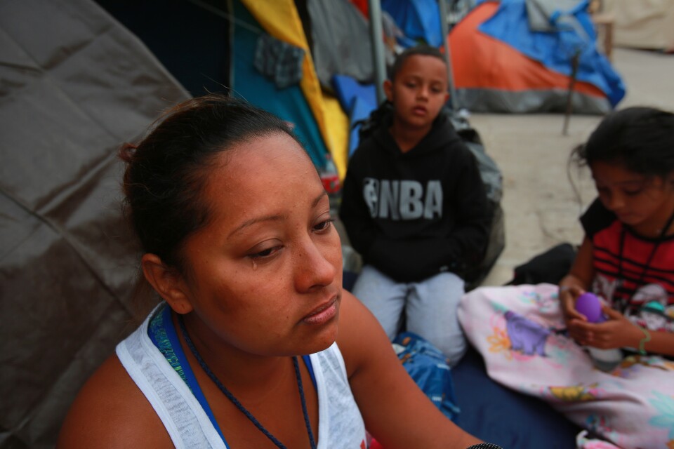Tijuana, BAJA CALIFORNIA, Mexico - December 16, 2018.   At the El Barretal temporary migrant shelter in Tijuana, Abigail Thompson Maldonado from Honduras, talks about the journey she and her husband and their three children made to reach this spot. In the background are Luis Antonio, 9, and Alexandra, 11, listen.

 In Tijuana, Mexico, children members of the migrant caravan are learning to live in limbo as they move between shelters, settling in as much as possible to create a sense of normalcy, with help from NGOs, counselors and aid organizations. (Photo by Peggy Peattie)