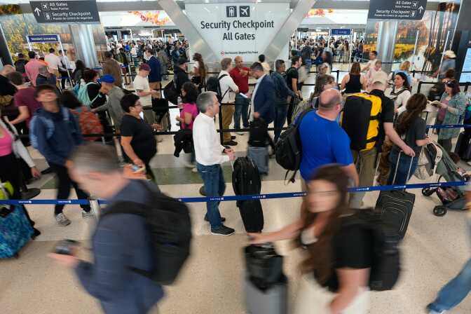 People waiting in a line that zig zags around in the airport near large signage that reads "Security checkpoint. All gates."
