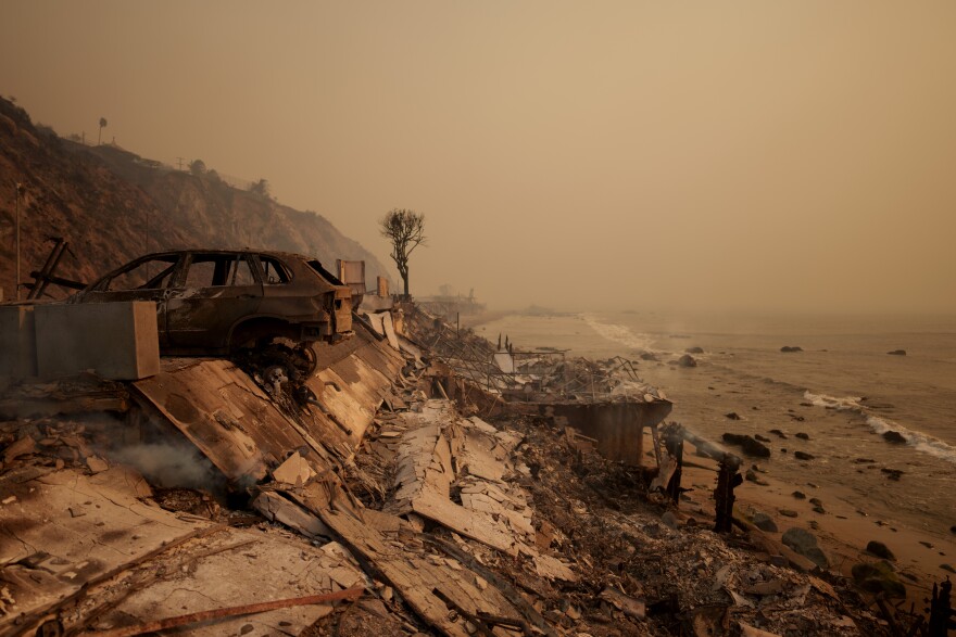 A hazy sky and sea has a burned car in the foreground.