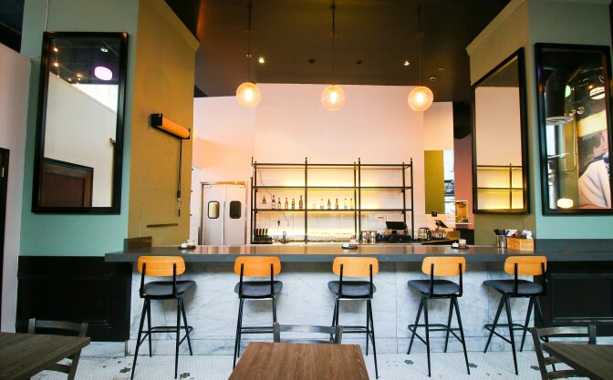 A row of 5 stools that are black with blond wood backs line the counter of what appears to be a bar in the making at a restaurant 