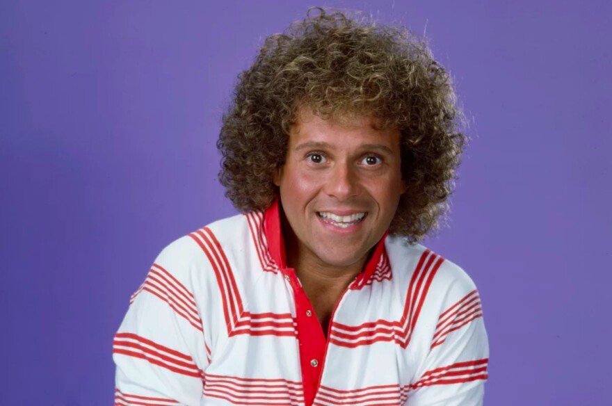 A man staring at the camera with a red stripped shirt and a light brown colored afro like hairdo