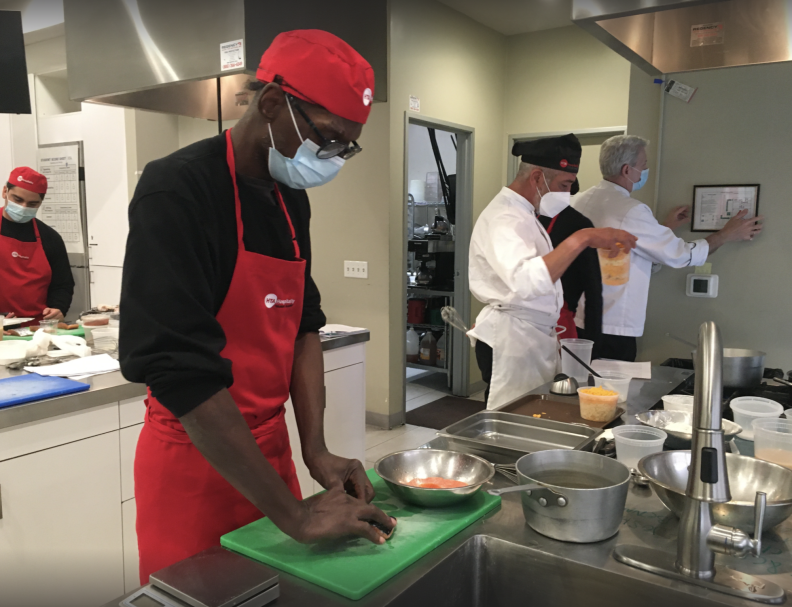 A man in a red cap and apron cooks in a commercial kitchen.