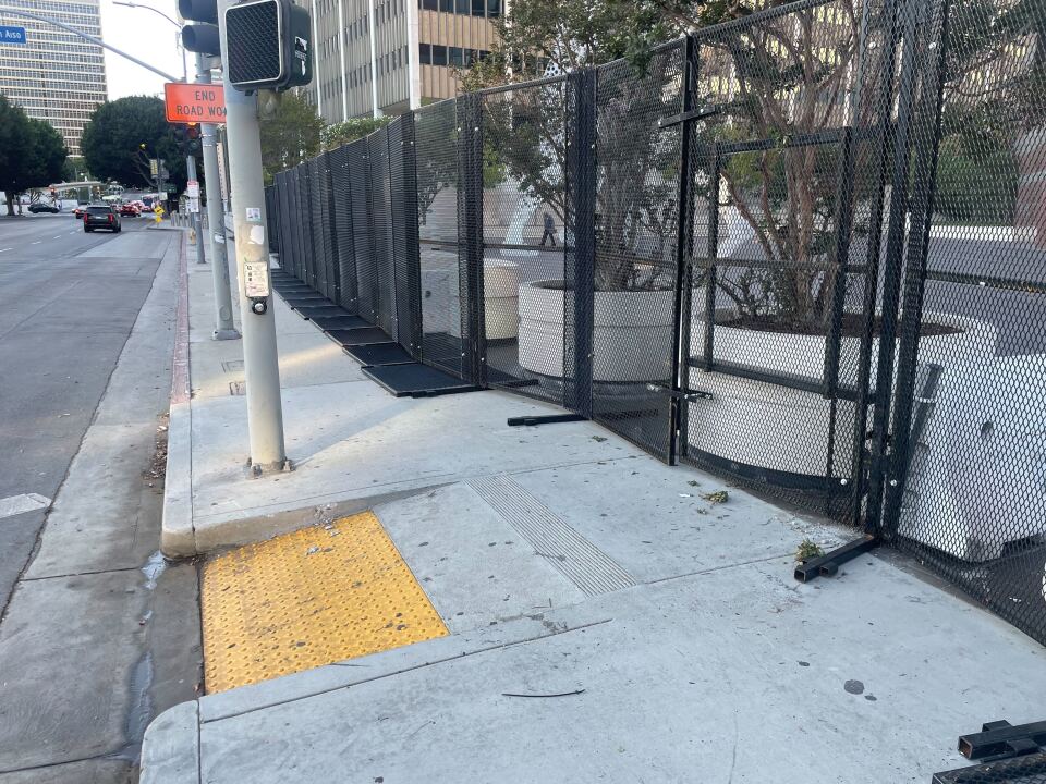 A photo of black metal fencing and a pedestrian curb onramp on a sidewalk. There are a few feet of room between the fencing and the ramp.