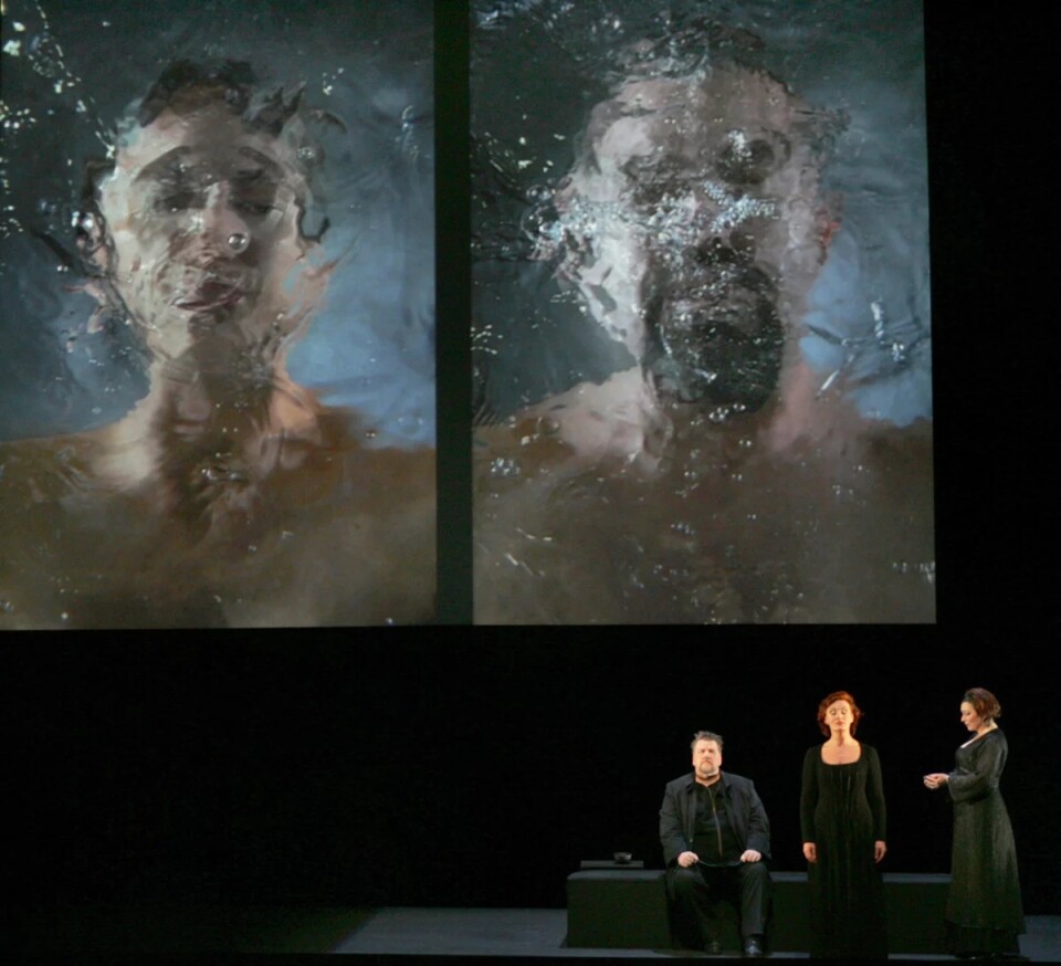 An image from Bill Viola's Tristan Project in which it depicts a man and woman in big water tanks and three people on the bottom right side of the image 