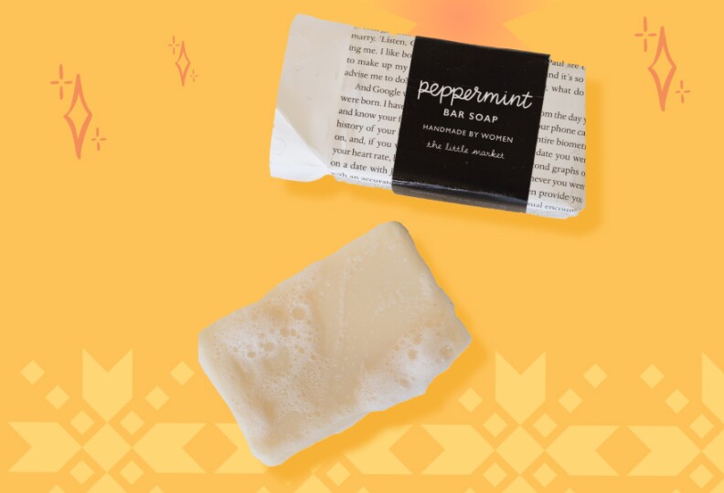 A bar of soap with soap bubbles on it is places next to its black and white packaging