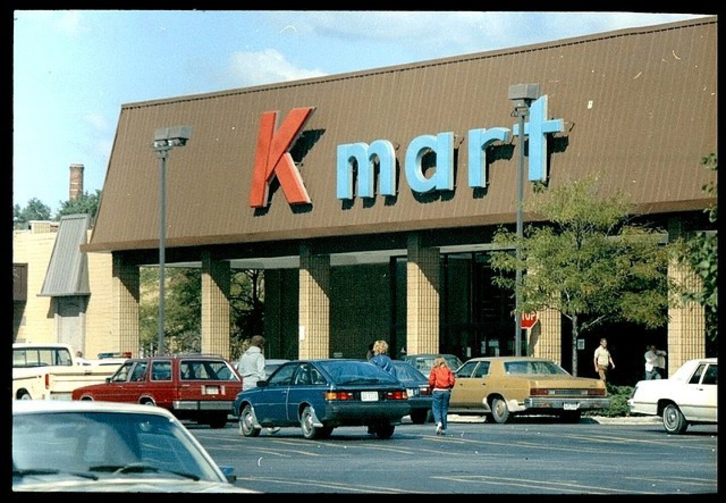 The outside of a vintage Kmart has cars parked in the lot and a red and blue sign on the facade.