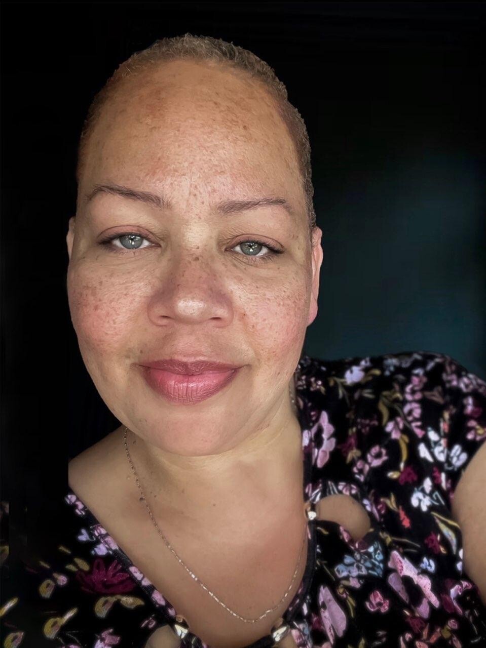 An image of a woman's face. She has short hair and wears a floral shirt. 