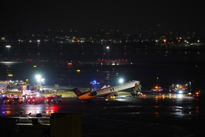 A plane with it's nose in the air is on the runway of an airport at night. Emergency vehicles surround the plane