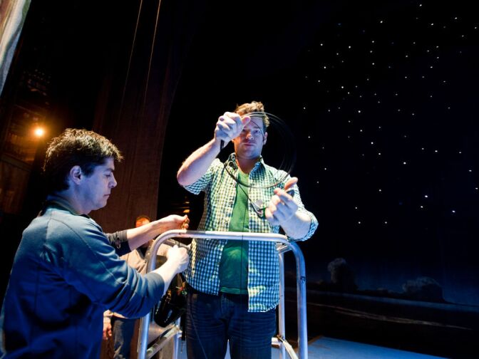 Flying choreographer Paul Rubin, left, and associate flyer Jimmy Little prepare to attach wires above the stage, from which the rig will hang.