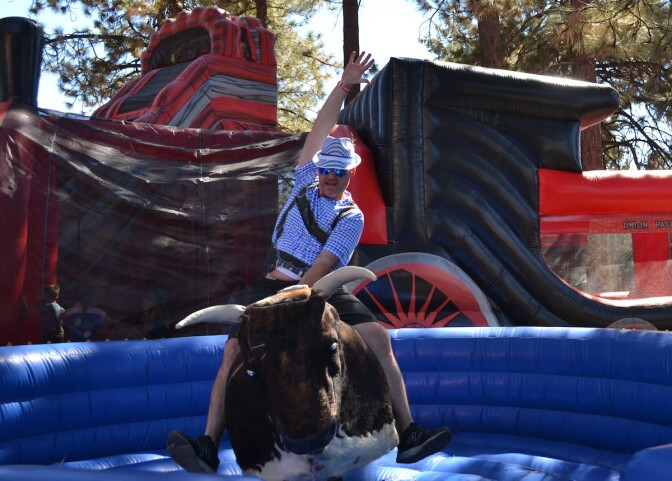 a man in German lederhosen rides a mechanical bull in what looks like a large inflatable pool