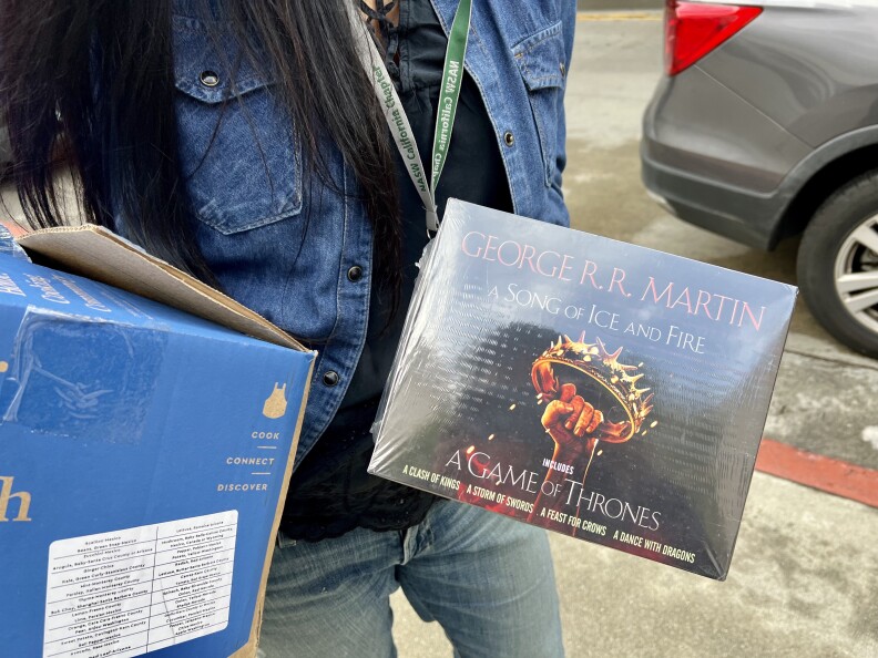 Sanati holds two boxes of books — one is a black box with Game of Thrones on it, and a photo of a hand holding a gold crown.