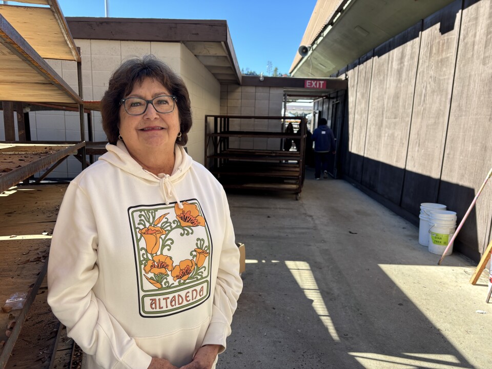 A woman wearing an Altadena hoodie stands in a work area, and smiles for the camera. 