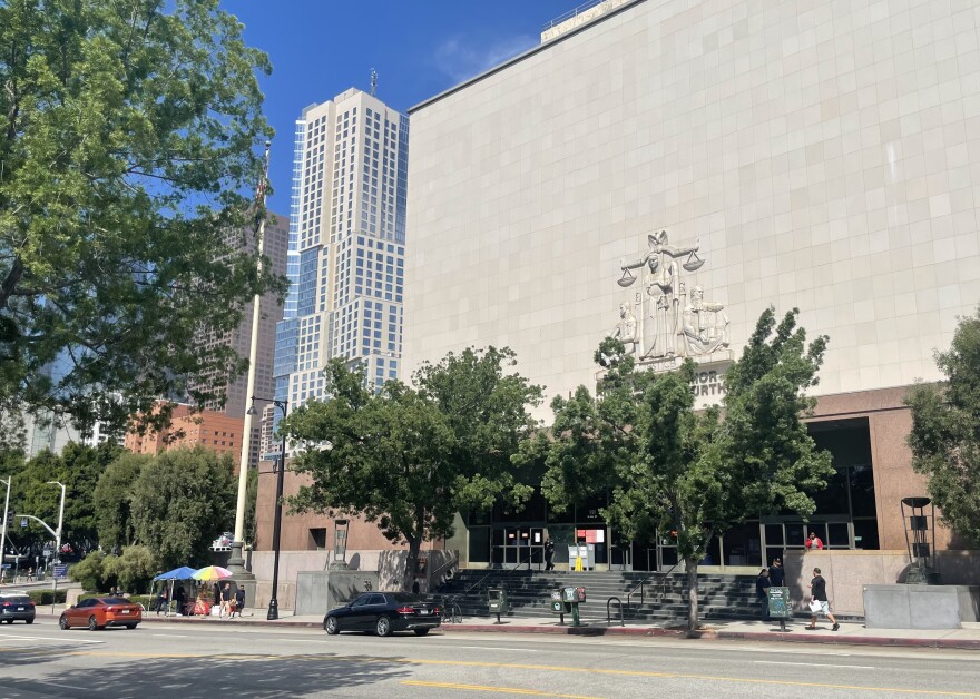 Exterior view of a court building in downtown Los Angeles, where trees line the sidewalks, with skyscrapers in the background.