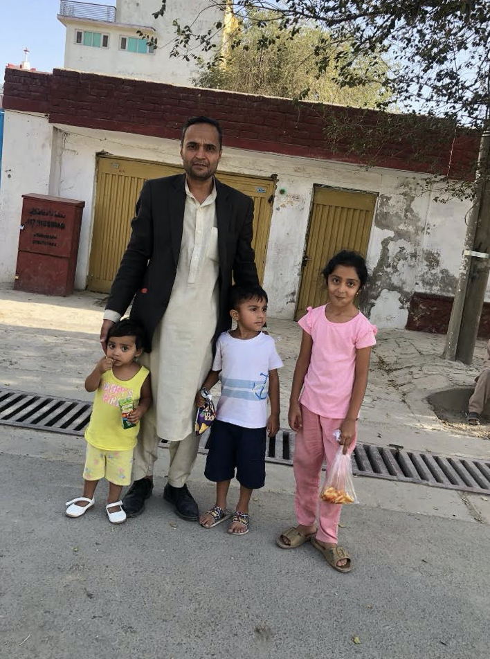 A man stands with three young children on a street in Kabul, Afghanistan with a white building behind them.