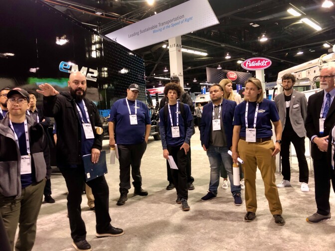 A diverse group of people stand in a well-lit convention center with lanyards around their necks.