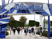 People walk under a blue and white sign that reads Disneyland Resort.