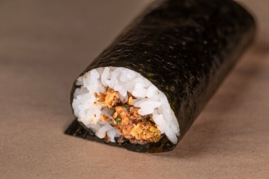 A well-prepared handroll is displayed on a light brown surface. 