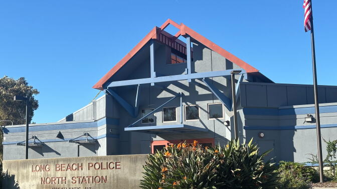 A concrete sign reads "Long Beach Police North Station" in front of a building with a peaked roof overhang and U.S. flag on a tall pole.