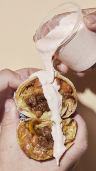Sauce is drizzled over a burrito being held with two hands.