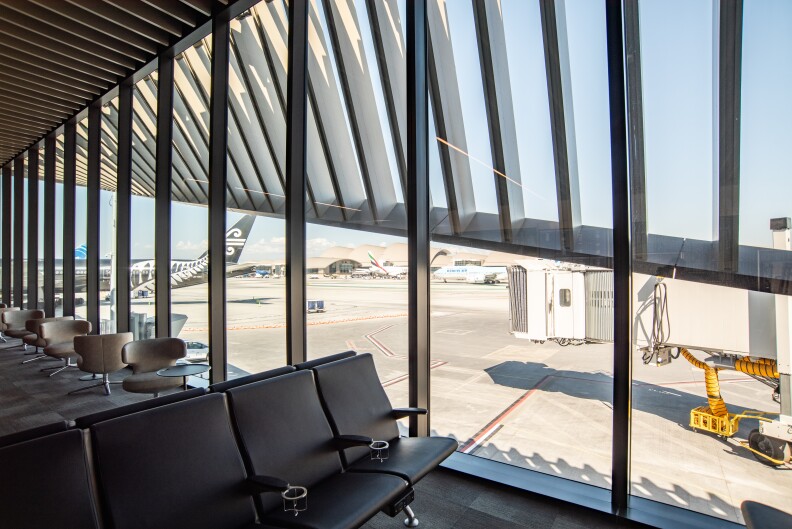 A window view on the tarmac from the new Midfield Satellite Concourse South. A row of pristine new black seats are seen.