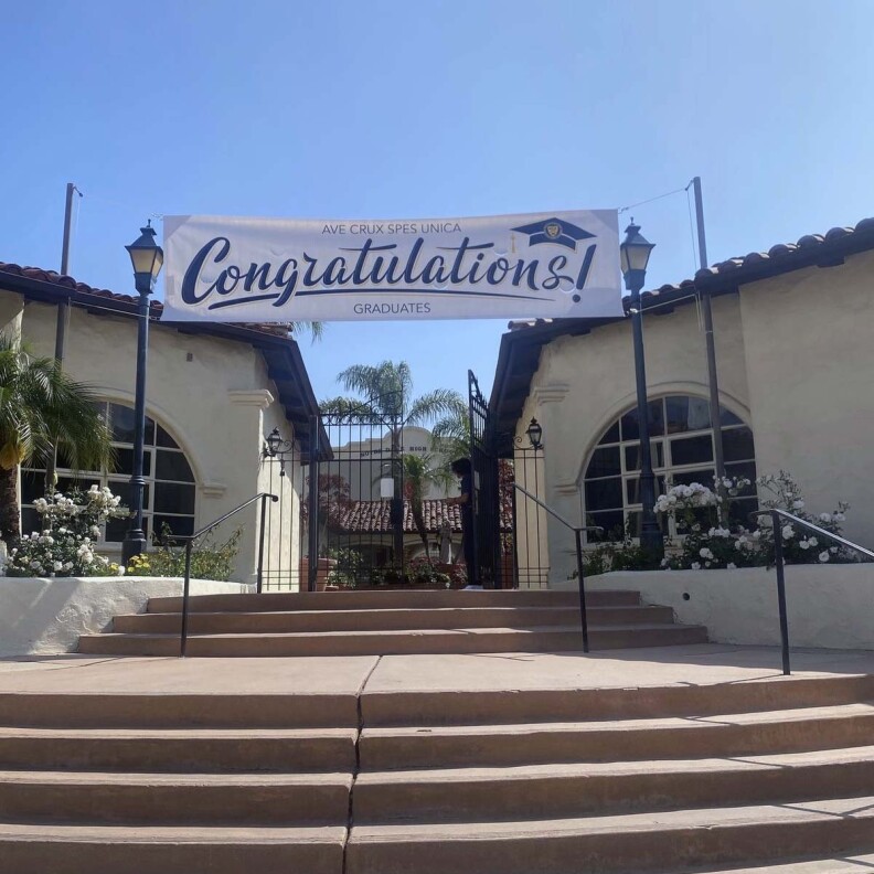 A concrete stairway with eight steps leads to an iron gate between two buildings, a banner draped between the buildings, above the gate, reads "Congratulations".