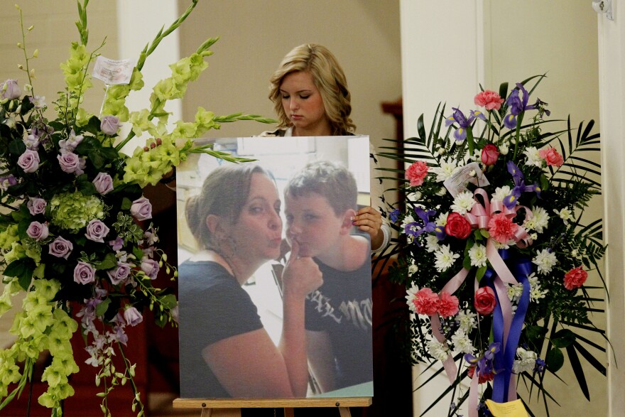 Hannah Anderson stands behind a poster-sized image of her mother and young brother, flanked by two large floral arrangements.