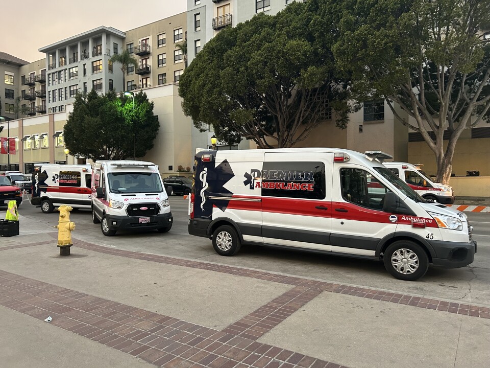 Three private ambulances are parked in a row on a street along a sidewalk 