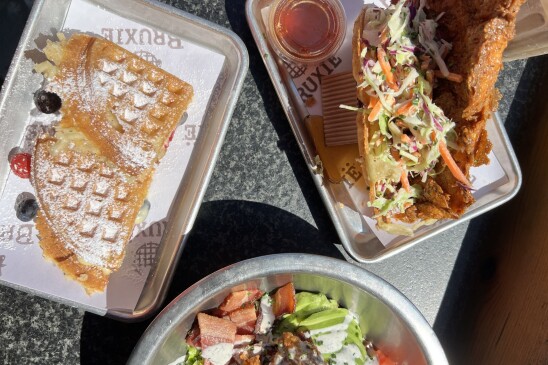 Three containers of food. Waffles, fried chicken and coleslaw, and a salad, all served in metal dishes. 