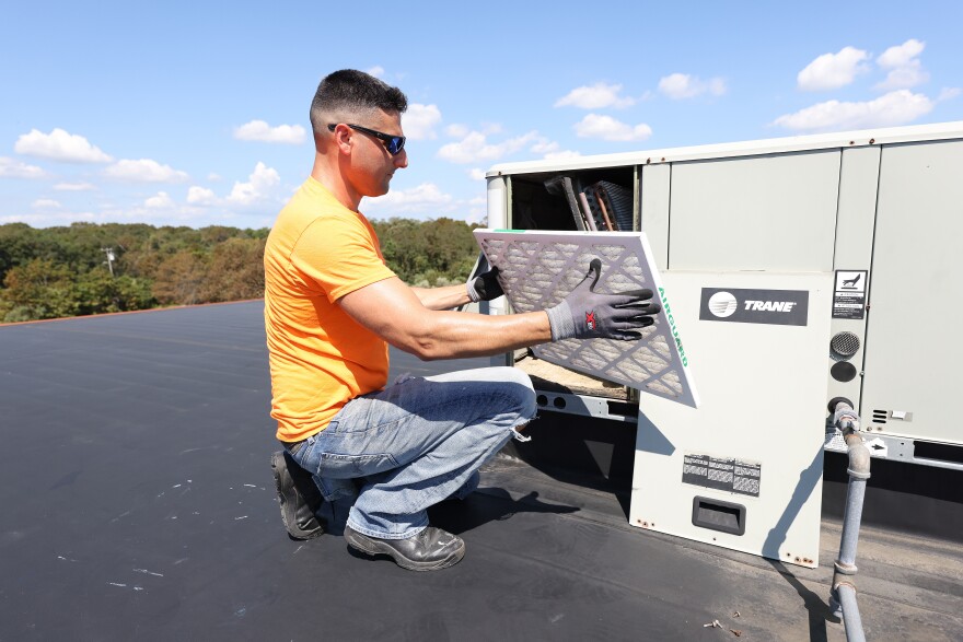 A person in an orange T-shirt places a new filter into an air conditioning unit.