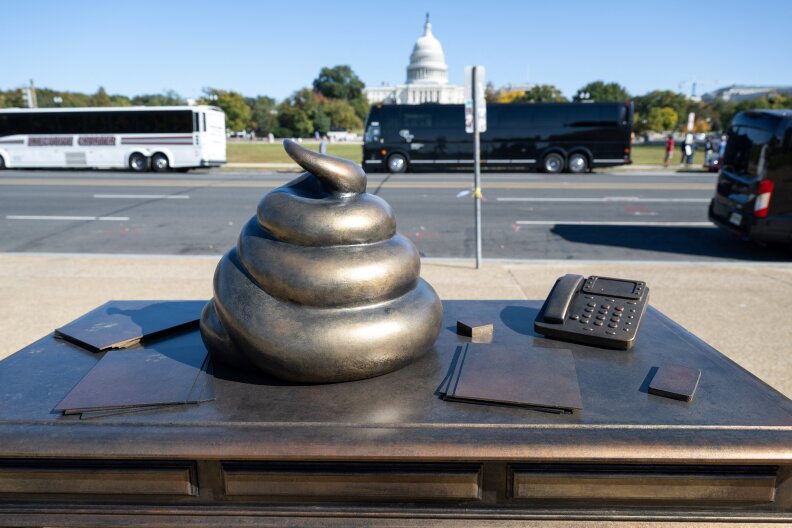 A bronze scupture of what appears to be a poop emoji on a desk has the U.S. Capitol in the background.