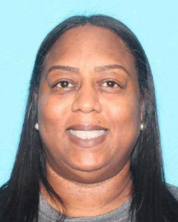 A woman with medium-tone skin smiles in a photo with a blue background.
