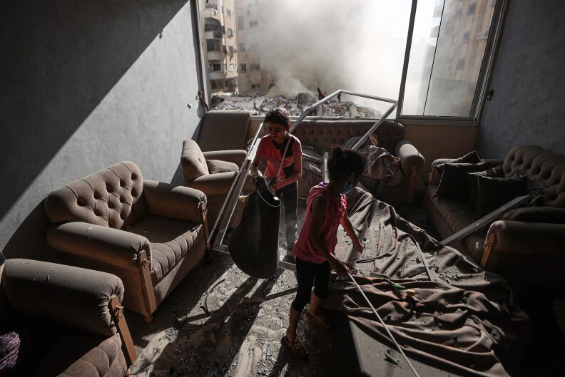 Two children are inside a bombed out home with blown out windows and debris