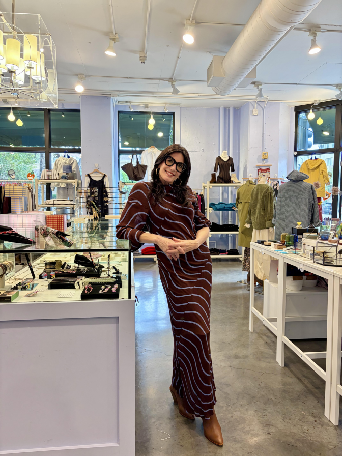 A white woman in a burgundy dress stands in front of a jewelry counter inside a shop.