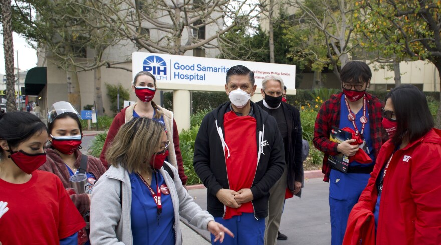 Nurses wearing red union face masks rally in front of PIH Good Samaritan Hospital. Some wear red shirts, others wear blue scrubs.
