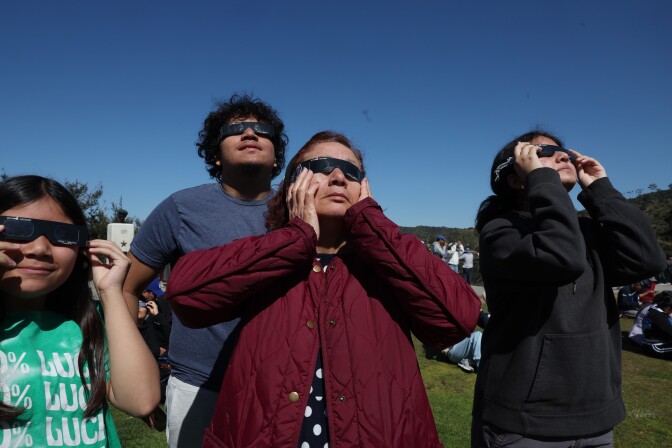 A family stands wearing eclipse glasses and looking up at the sky. 