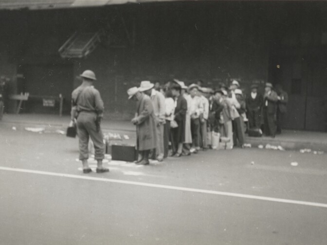 Japanese Americans lined up and under guard on Central Avenue in Los Angeles. They were transported to Santa Anita Race Track (Santa Anita Assembly Center), ca. April 1942.