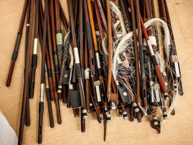 Broken bows rest in a pile on a table at the Music Repair Shop.