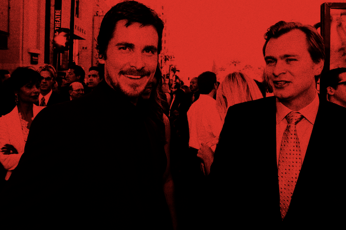 Christian Bale and Christopher Nolan are standing outside, wearing suits. Christian Bale smiles into the camera and Christopher Nolan is looking to the side. A large crowd of people stretches to the horizon of the image. This image has a red filter over it.
