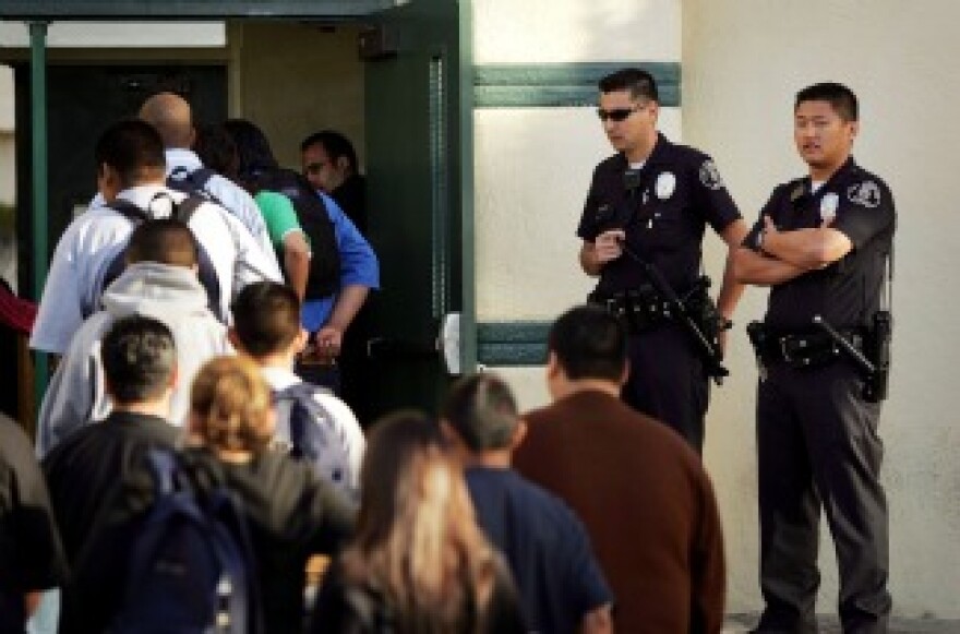 Los Angeles School Police officers watch students lining up to pass through a security check point on April 21, 2005, in the aftermath of two apparent racially motivated student brawls at Thomas Jefferson High School.